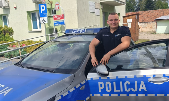 policjant stoi przy radiowozie policyjnym, w tle budynki