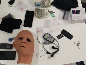 na stole leżą zabezpieczone przedmioty: gumowa maska, telefony komórkowe, pieniądze, klucze