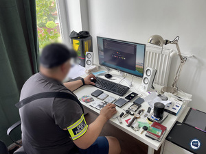 funkcjonariusz cbzc siedzi przy stanowisku komputerowym, na stoliku leżą różne drobne przedmioty zabezpieczone przez policjantów: nośniki pamięci, zegarek, dowody tożsamości