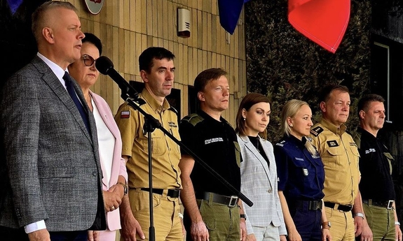 Funkcjonariusze stoją obok ministra spraw wewnętrznych i administracji, który przemawia stojąc przy statywie z mikrofonem