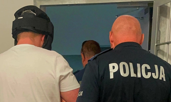 Zdjęcie przedstawia zatrzymanego mężczyznę w kasku, obok stoi policjant