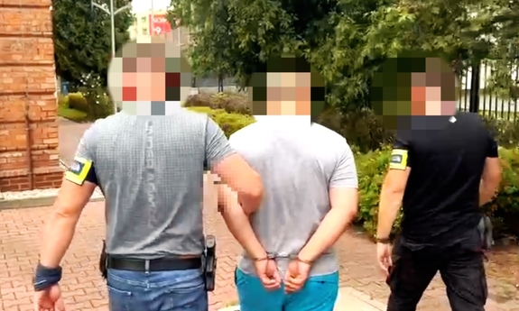 dwaj nieumundurowani funkcjonariusze prowadzą zatrzymanego mężczyznę zakutego w kajdanki