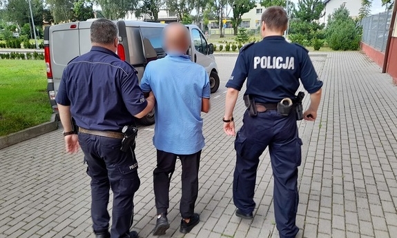 dwaj policjanci z zatrzymanym mężczyzną zakutym w kajdanki