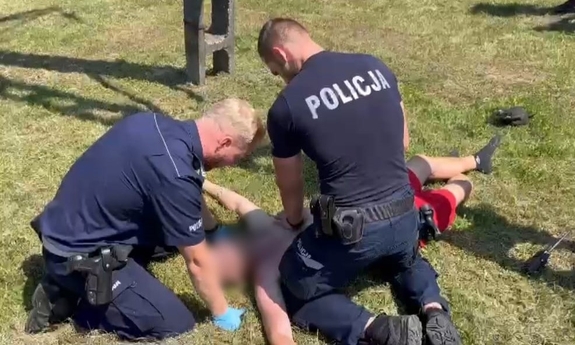 dwaj policjanci reanimują mężczyznę leżącego na ziemi obok słupa energetycznego