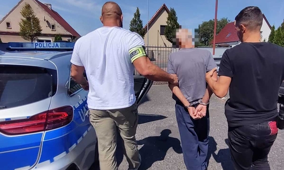 dwóch policjantów prowadzi zatrzymanego mężczyznę do radiowozu