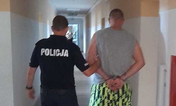 policjant prowadzi zatrzymanego zakutego w kajdanki