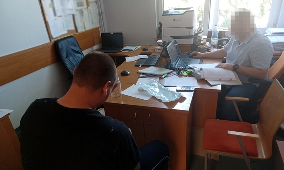 zatrzymany siedzi na krześle skuty w kajdanki podczas przesłuchiwania przez policjanta