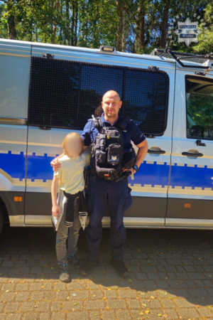 policjant stoi przy radiowozie w mundurze, obok niego stoi dziecko