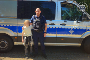 policjant stoi przy radiowozie w mundurze, obok niego stoi dziecko