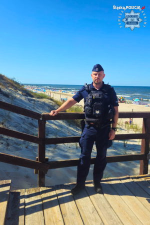 policjant w mundurze stoi na pomoście prowadzącym na plażę widoczną w głębi