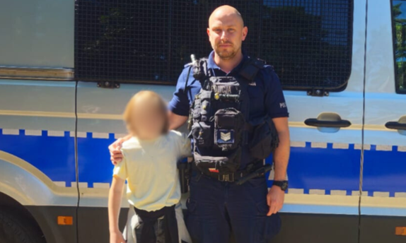 policjant stoi przy radiowozie w mundurze, obok niego stoi dziecko