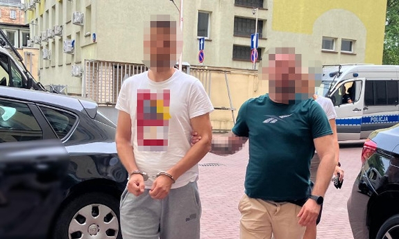 funkcjonariusz prowadzi zatrzymaną osobę zakutą w kajdanki