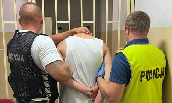 dwaj funkcjonariusze z zatrzymanym mężczyzną zakutym w kajdanki