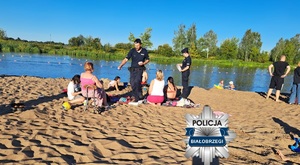 Policjanci rozdają ulotki profilaktyczne osobom przebywającym na plaży.