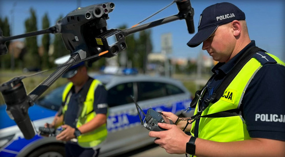 umundurowany policjant steruje dronem, w tle funkcjonariusz i radiowóz