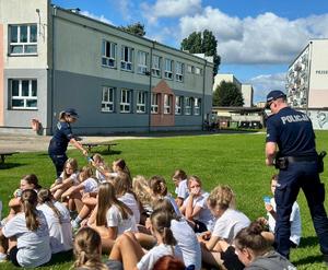 Policjanci rozdają ulotki profilaktyczne grupie młodzieży.
