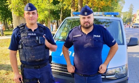 na zdjęciu umundurowani policjanci stoją na tle radiowozu