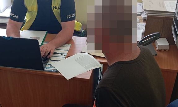 policjant siedzi przy biurku, obok siedzi zatrzymany