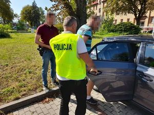dwóch policjantów prowadzi zatrzymanego mężczyznę do radiowozu