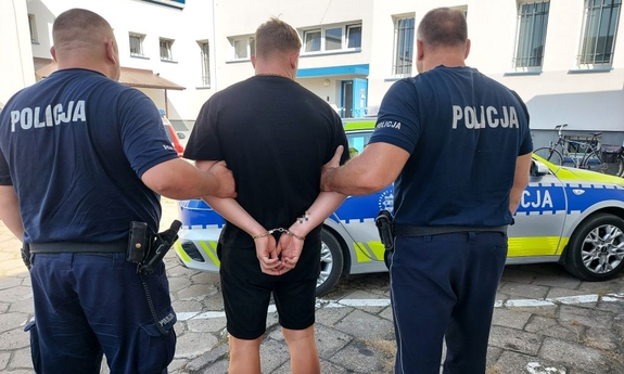 dwóch umundurowanych policjantów prowadzi zatrzymanego mężczyznę