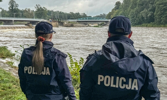 policjant i policjantka patrzą na rzekę stojąc na jej brzegu