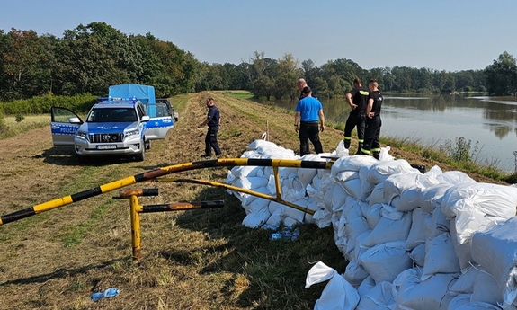 policjanci i strażacy na wale, na którym leżą worki z piaskiem