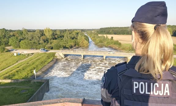 policjantka stoi na moście, na dole płynie woda i stoi radiowóz