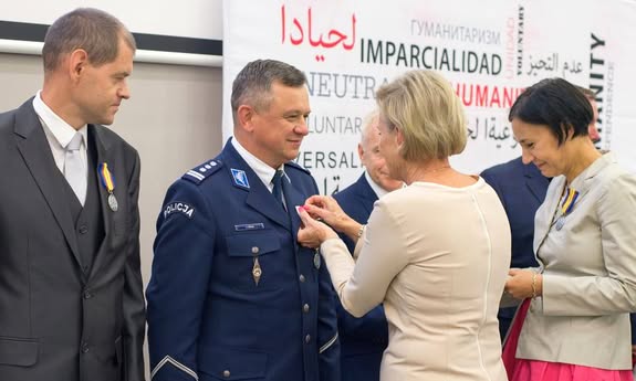 KOBIETA PRZYPINA ODZNAKĘ MĘŻCZYŹNIE
