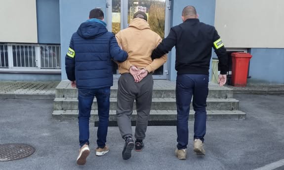 policjanci idą z zatrzymanym do budynku