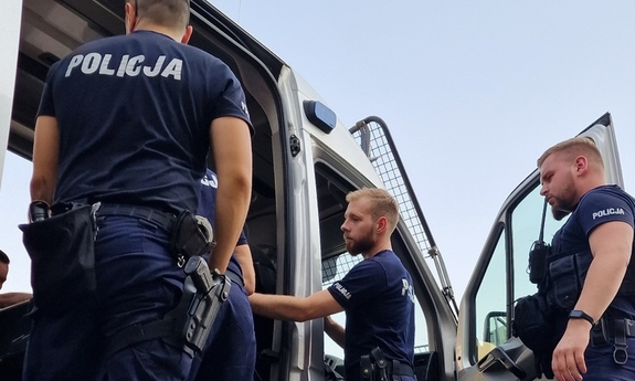 trzej policjanci stoją przy radiowozie
