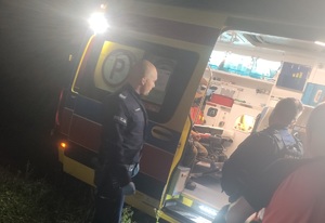 na zdjęciu umundurowani policjanci stoją przy karetce pogotowia