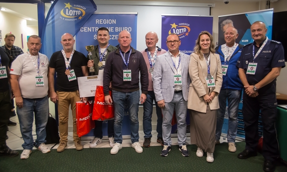 Na zdjęciu uczestnicy zawodów strzeleckich pozują do zdjęcia na tle niebieskiej ścianki.