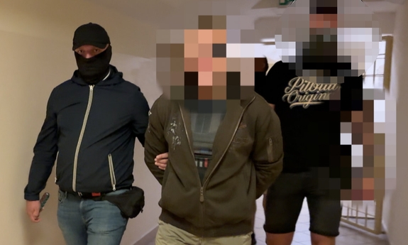 Dwaj funkcjonariusze prowadza zatrzymanego korytarzem.