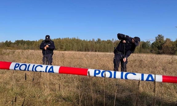 Funkcjonariusze na trawiastym terenie w trakcie poszukiwań. Na pierwszym planie taśma z napisem Policja odgradzająca teren.