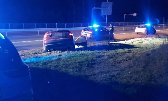 Na zdjęciu dwa oznakowane radiowozy, samochód służbowy na ulicy i pojazd, którym kierowca uciekał przed kontrolą drogową. Obok samochodu stoi policjant.