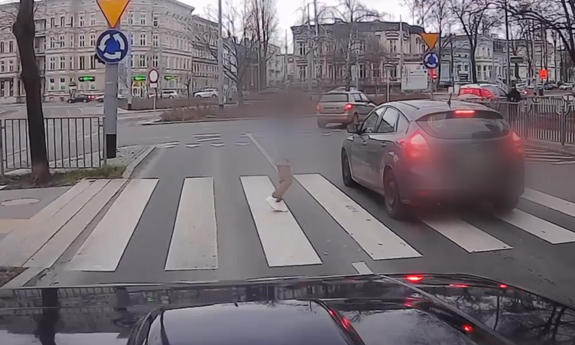 Na zdjęciu zarejestrowane wykroczenie drogowe. Mężczyzna przechodzi przez pasy, przed nim przejeżdża samochód.