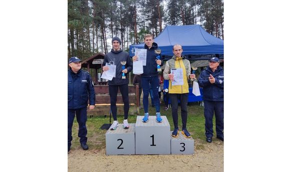 Na podium laureaci. Obok po jednej i drugiej stronie podium stoi policjant.