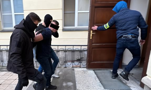 policjant otwiera drzwi przed innymi policjantami idącymi z zatrzymanym