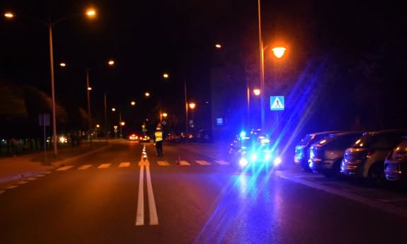 noc, policjant stoi na przejściu dla pieszych