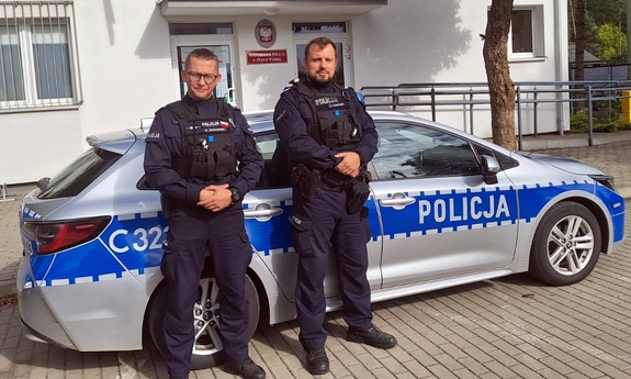 Dwaj policjanci stojący przy radiowozie policyjnym.