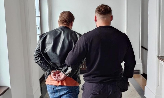 Funkcjonariusz prowadzi zatrzymanego mężczyznę korytarzem.