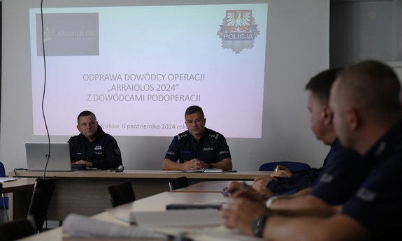 Policjanci podczas odprawy siedzą przy stołach.
