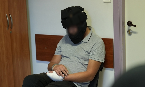 zatrzymany siedzi na krześle z kaskiem ochronnym na głowie