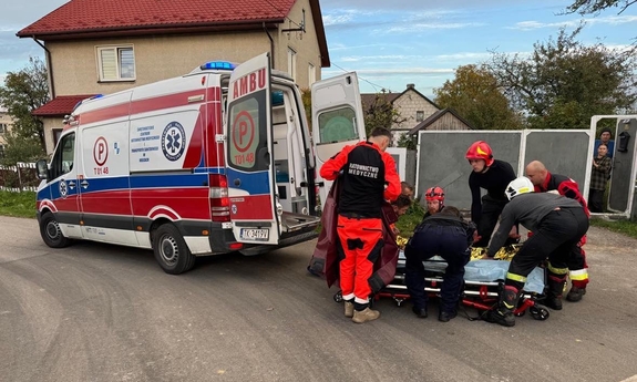 Na zdjęciu ratownicy pogotowia i strażacy pomogą w transporcie kobiety na noszach do karetki.
