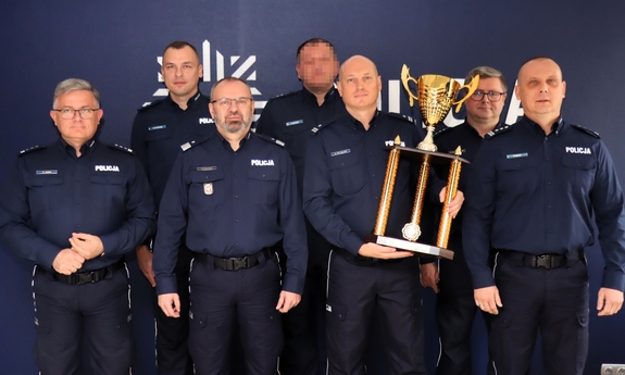 Grupa policjantów pozuje do zdjęcia, jeden z nich trzyma trofeum.