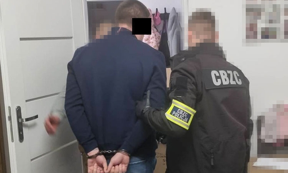 Funkcjonariusz CBZC prowadzi zakutego w kajdanki mężczyznę.