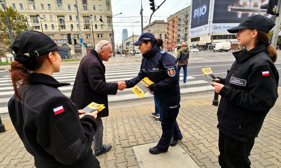 Policjantka i dwie uczennicy klasy mundurowej podczas rozdawania ulotek na ulicy.