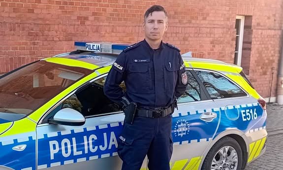 policjant stoi przed radiowozem.