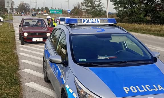 na pierwszym planie stoi radiowóz, w tle wiśniowy volkswagen.