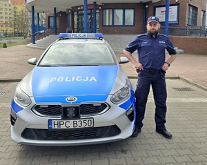 policjant stoi obok radiowozu.
